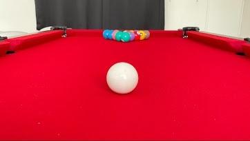 Sala de jogos com mesa de bilhar profissional, bolas coloridas posicionadas, jogo de dardos ao alvo, dominó, baralhos, Uno e Super Trunfo